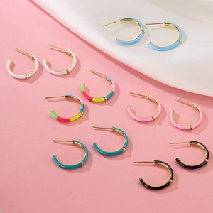 Colorful enamel C-shaped gold-tone hoop earrings set against a soft pink backdrop