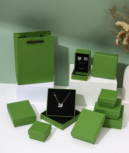 Green jewelry gift boxes and matching paper bags set on white geometric display stands