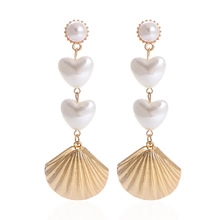 Detailed view of long gold earrings featuring heart-shaped pearls and shell pendants