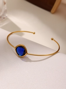 Detail view of a square blue glass gemstone set in a minimalist gold stainless steel bangle