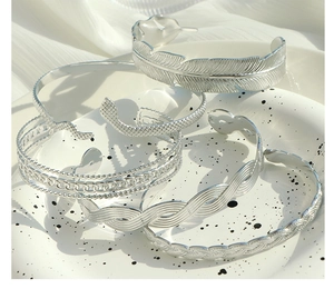 Macro shot of silver feather texture and braided chain bracelets on white plate