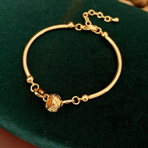 Detail of 18K gold plated bamboo link bracelet with hollow ball charm on green velvet