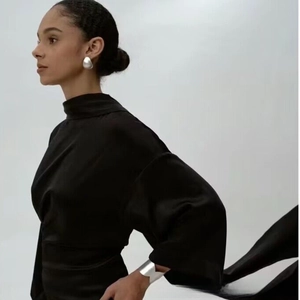 Gros plan sur le tissu satiné noir de la robe et les bijoux métalliques superposés