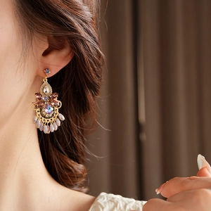 Macro shot of gold vintage teardrop earrings with purple crystals and beige beaded tassels