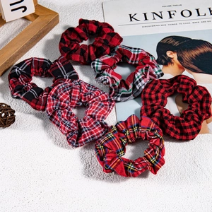 Set of six red and black plaid fabric scrunchies arranged on a white textured surface
