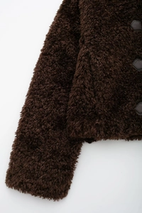 Close-up of fluffy faux fur texture and hexagon leather buckle on dark brown coat