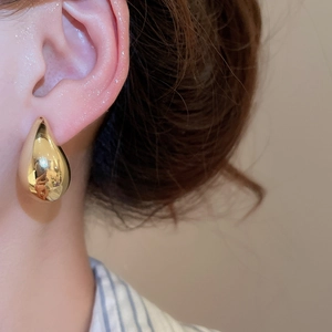 Close-up of a model wearing a polished gold water drop earring with a sleek C-shape finish