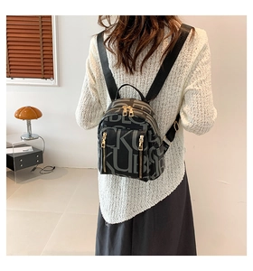 Close-up of black backpack with repeating letter pattern and gold zipper details on model