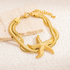 Detail einer zweischichtigen goldenen Schlangenkette mit Seestern-Anhänger auf Marmor