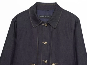 Détail de surpiqûres contrastées et boutons dorés sur veste en jean bleu foncé