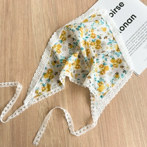Detailed flat lay of white lace floral headscarf with yellow flowers on wooden surface