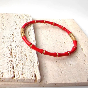 Macro detail of red bamboo-style bangle with 18k gold plating on stone surface