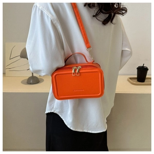 Orange suitcase-shaped leather crossbody bag with golden zippers worn by a model