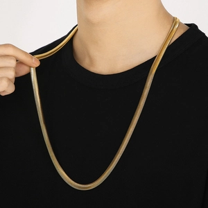 Close-up of gold flat snake bone chain necklace worn by a model on black background