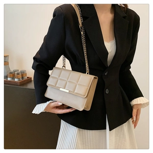 Close-up of beige quilted crossbody bag with gold chain strap on a model outfit