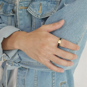 Close-up of a wide 8mm gold and black carbon fiber ring worn on a finger with denim jacket