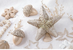 Assorted champagne gold Christmas ornaments including stars and snowflakes on white snow
