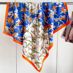 Gros plan détaillé d'un foulard en soie de 90cm avec motifs floraux et bordures orange vif