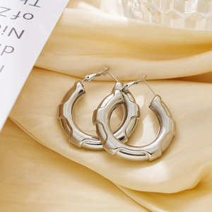 Macro shot of silver titanium steel C-shaped earrings on elegant satin fabric