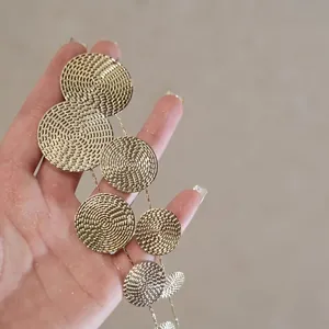 Close-up of golden long tassel earrings with spiral textured metal discs on chains
