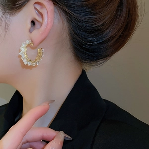 Close-up of C-shaped gold metal earrings wrapped with white crystals on a model