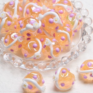 Macro shot of orange glass beads with purple dots and 3D white floral details