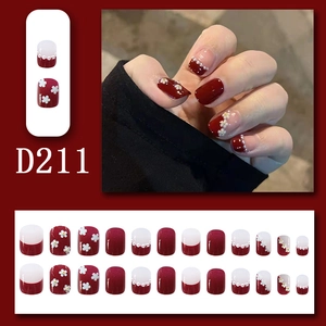 Detail of dark red press-on nails with white floral patterns and pearl accents