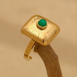 Macro detail of 18K gold plated square ring featuring a green gemstone on a wood stand