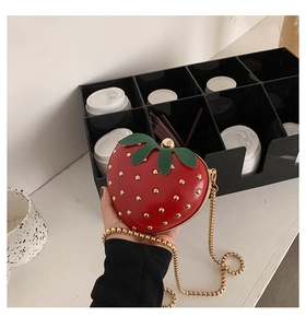 Detail of red strawberry crossbody bag with golden chain and green leaf accents