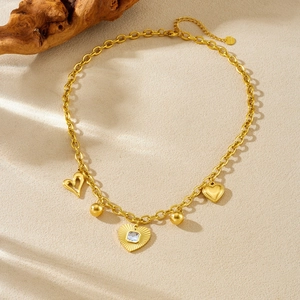 Collier en acier inoxydable doré avec pendentifs cœur et boule sur fond beige texturé