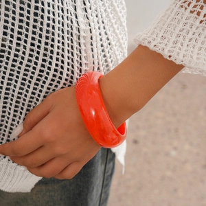 Close-up of a wide translucent orange resin bangle worn with a white knit sweater