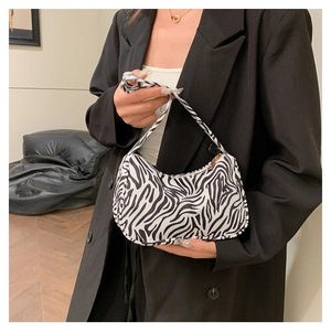 Détail d'un sac baguette en toile à motif zèbre tenu par un mannequin en veste noire