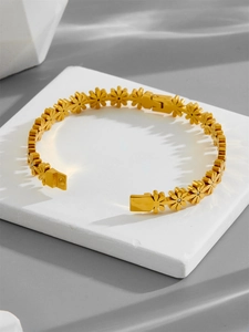 Close-up of gold daisy bracelet with crystal accents on a white stone background