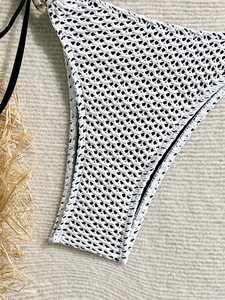 Detail of white crochet knit bikini bottom with black side ties and mesh pattern