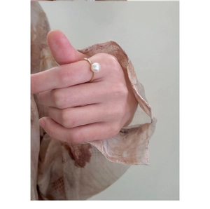 Close-up of elegant gold ring featuring a single pearl on model's hand with vintage vibe