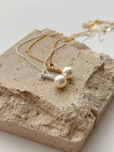 Close-up of gold and silver S925 necklaces with white pearls on a stone base