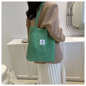 Close-up detail of green corduroy tote bag with vintage white square fabric patch label