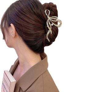 Elegant gold metal bow hair claw clip with pearl detail shown on a model's hair