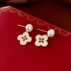 Macro detail of mother-of-pearl clover earrings with pearl accents on red display box