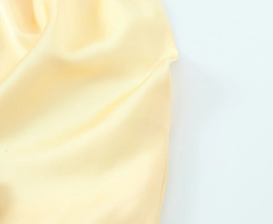 Gros plan sur un tissu satiné jaune pâle montrant une texture lisse et brillante