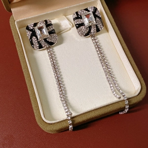 Detail of square silver needle earrings with crystal tassels and black enamel accents