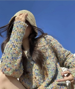 Close-up of a beige woven straw bucket hat styled with a colorful chunky knit cardigan