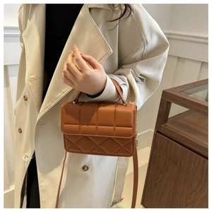 Detail of a brown embossed leather crossbody bag held by a model in a beige coat