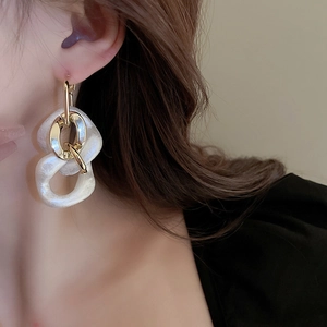 Close-up of golden metal chain earring with white acrylic hoop worn on a model's ear