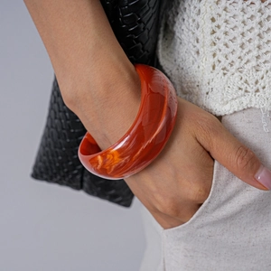 Detail of chunky acrylic red amber resin bangle with swirl pattern on woman's wrist