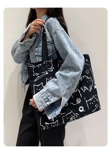 Detailed view of the large black canvas tote bag with white cat prints on a female model