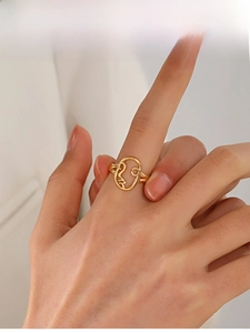 Detail view of gold plated stainless steel ring with abstract face design on finger