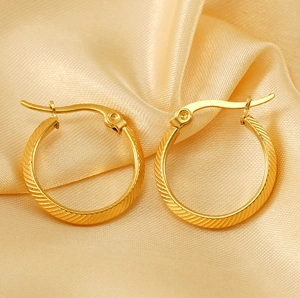 Detailed view of gold plated striped hoop earrings on elegant champagne satin fabric