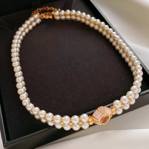 Détail d'un collier de perles à double rang avec fermoir doré et gemme rose en coffret
