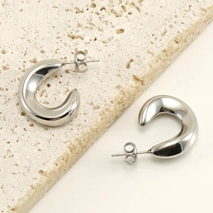 Close-up of silver C-shaped polished stainless steel earrings on a beige stone base
